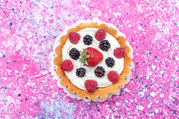 Вид сверху крупным планом вкусного сливочного торта с разными ягодами на фиолетовом ярком, фруктово-ягодном пироге цвета выпечки