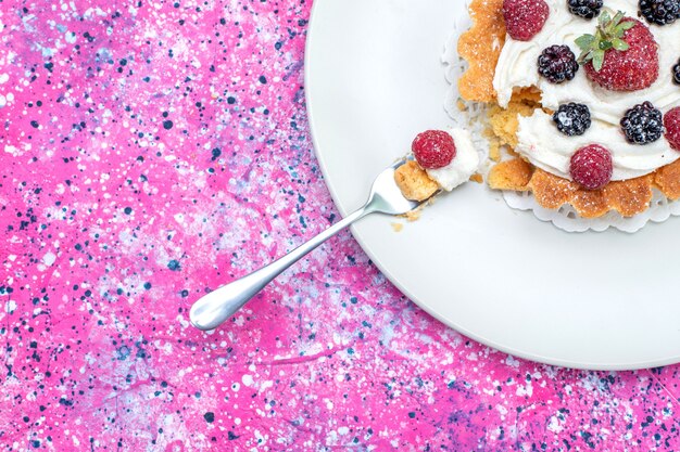 Top close view of delicious creamy cake with different fresh berries inside plate on bright, berry fruit color fresh