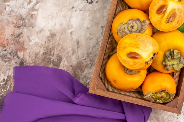 Top close view delicious persimmons in a wood box purple shawl on nude background