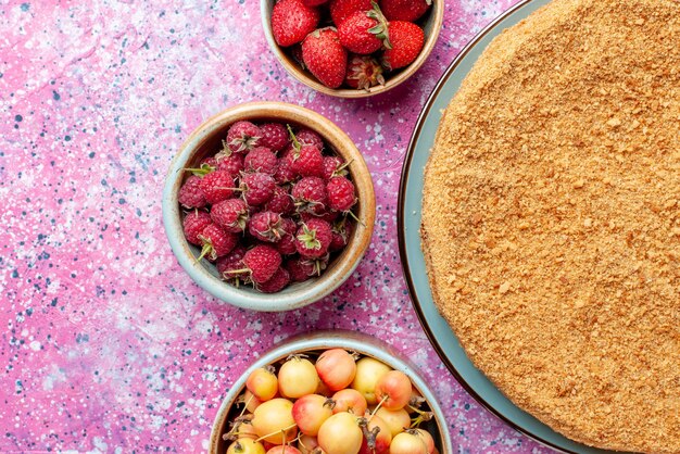 Top close view delicious round cake inside plate with fruits on the bright pink desk cake pie biscuit sweet bake sugar