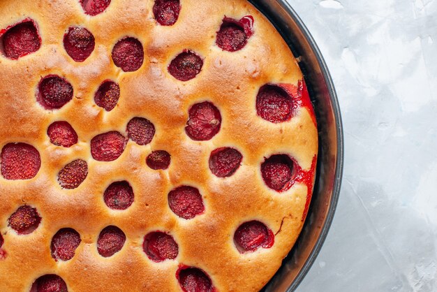 Top close view of delicious strawberry cake baked with fresh red strawberries inside with pan on light-white desk, cake biscuit fruit sweet dough bake