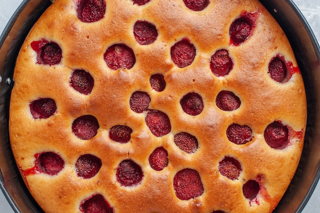 Top close view of delicious strawberry cake baked with fresh red strawberries inside with pan on white desk, cake biscuit fruit sweet