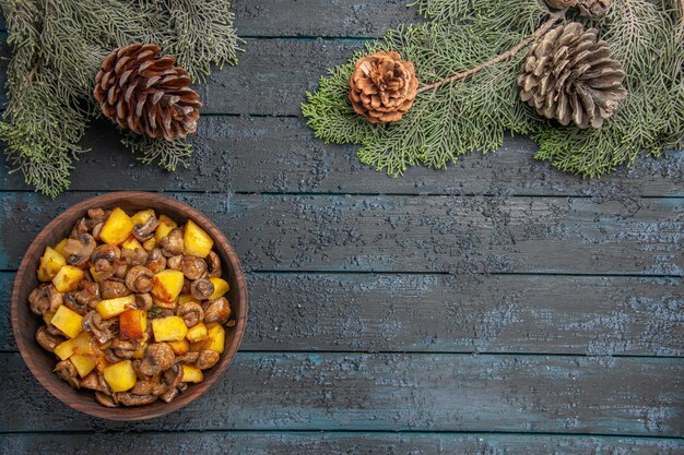 Top close view dish and branches dish of mushrooms and potatoes on the left side of the grey table under the spruce branches