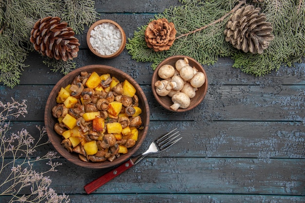 Top close view dish and branches plate of mushrooms and potatoes on the grey table under the spruce branches with cones mushrooms and salt next to the fork