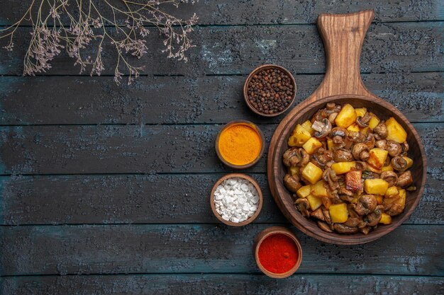 Top close view dish and spices a dish of potatoes and mushrooms on the cutting board and a notebook and colorful spices around it