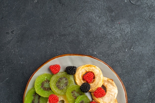 Вид сверху крупным планом сушеные кольца ананаса с сушеными киви и яблоками на темно-серой стене фруктовый сухой изюм сладкие сахарные конфеты