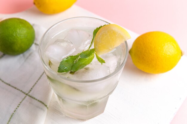 Top close view of fresh cold lemonade with ice inside glass along with fresh lemons on the pink surface