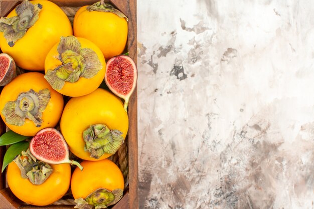 Top close view fresh persimmons figs in wooden box on nude background