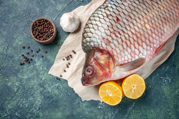 top close view fresh raw fish with pepper and lemon on dark-blue background