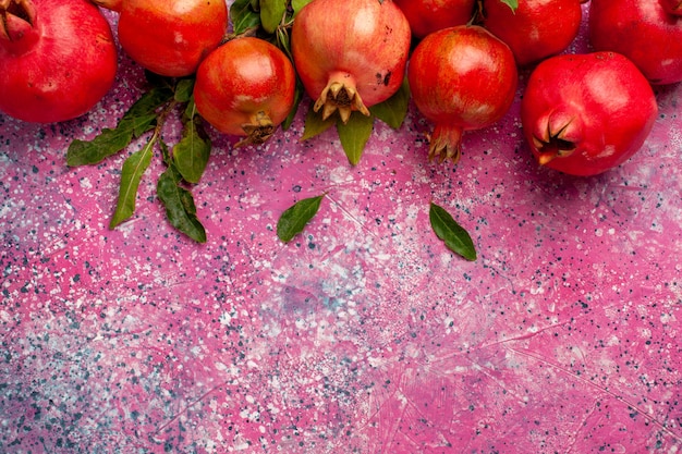 Top close view fresh red pomegranates with green leaves on pink wall fruit color fresh juice mellow