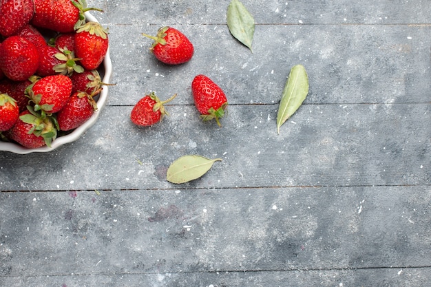 Top close view of fresh red strawberries inside white plate along with green dried leaves on grey , fruit fresh berry photo vitamine health