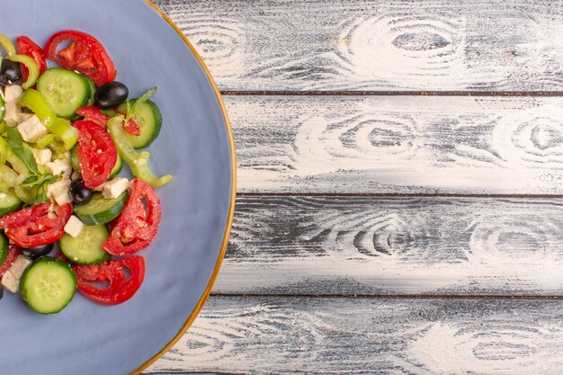Вид сверху крупным планом салат из свежих овощей с нарезанными огурцами помидоры оливковое внутри тарелки на сером фоне овощная еда салат цвет еды