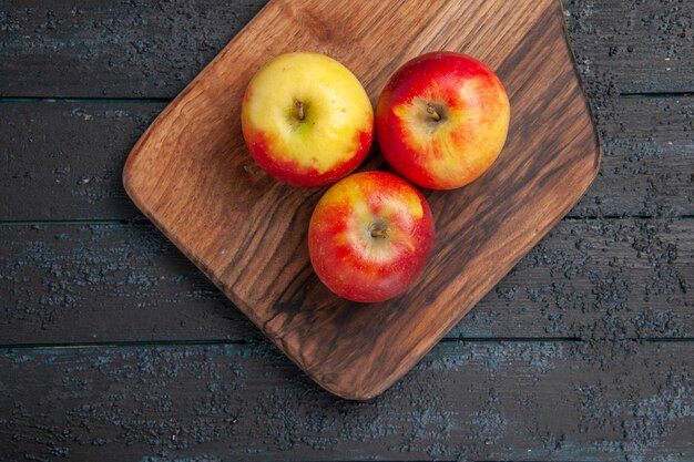 上部のクローズビューは、灰色のテーブルの上の木製のまな板に3つの黄赤リンゴを実らせます