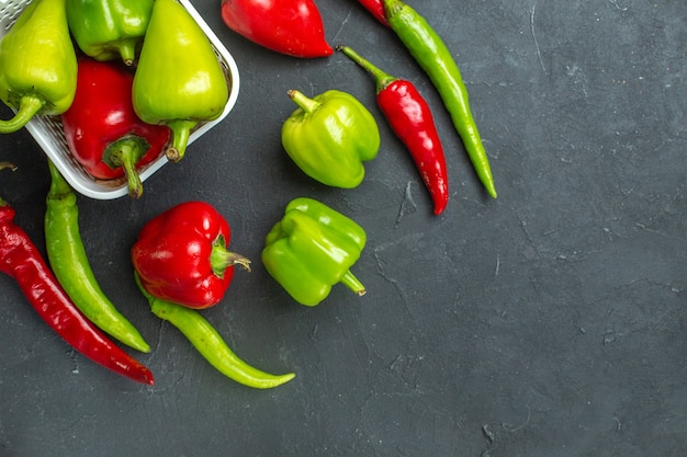 Top close view green and red peppers in plastic basket hot peppers on dark background free space