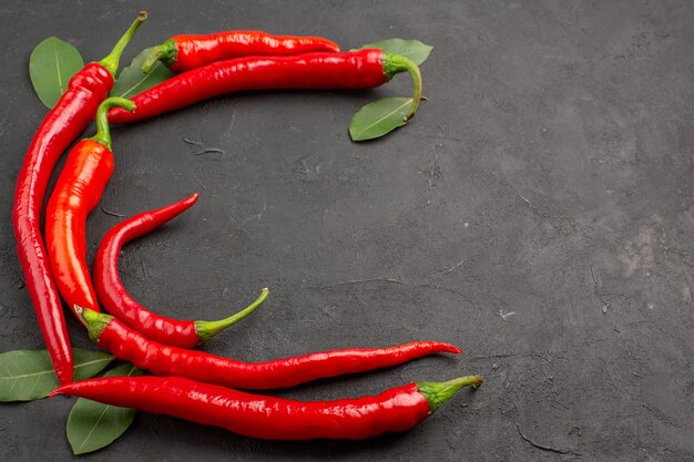 Top close view half circle of red hot peppers and bay leaves at the right side of the black table