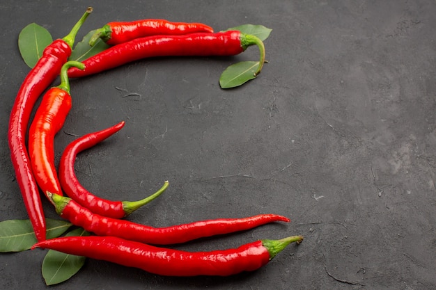 Top close view half circle of red hot peppers and bay leaves at the right side of the black table