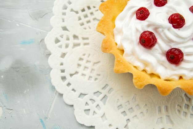 Top close view little delicious cake with cream and red cranberries isolated on the light surface 