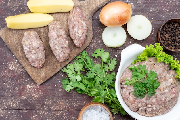 Top close view of minced raw meat with greens inside plate with onions raw potatoes salt on brown