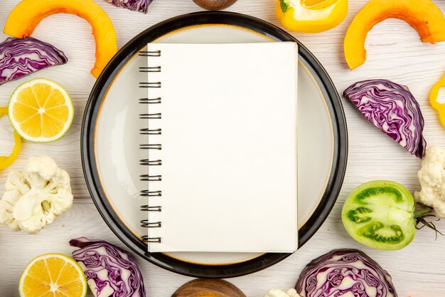 Top close view notebook on round platter cut vegetables different spices in small bowls on wooden surface