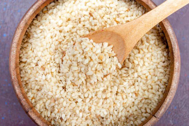 Top close view raw groats inside round brown pot on dark background.