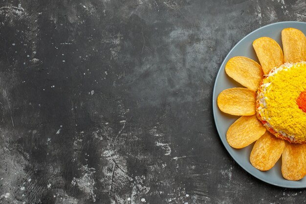 Top close view of salad with chips around on plate on dark background