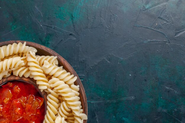 Top close view shaped italian pasta with tomato sauce on dark-blue surface