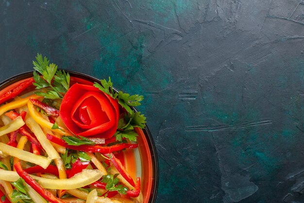 紺色の表面のプレート内のスライスしたピーマンの異なる色の野菜サラダを上から見る