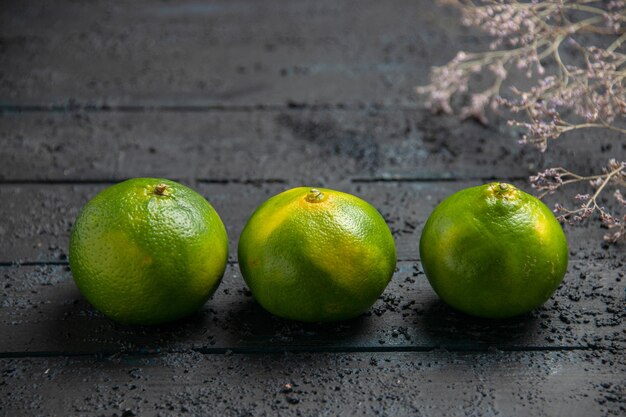 Top close view three limes three green-yellow limes next to branches on the dark background