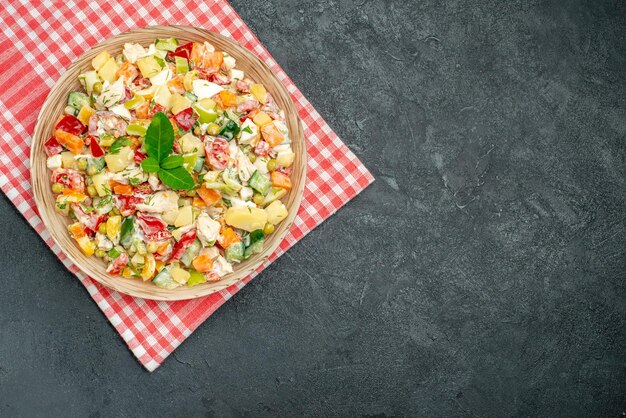 Top close view of vegetable salad in bowl on red napkin on dark grey background