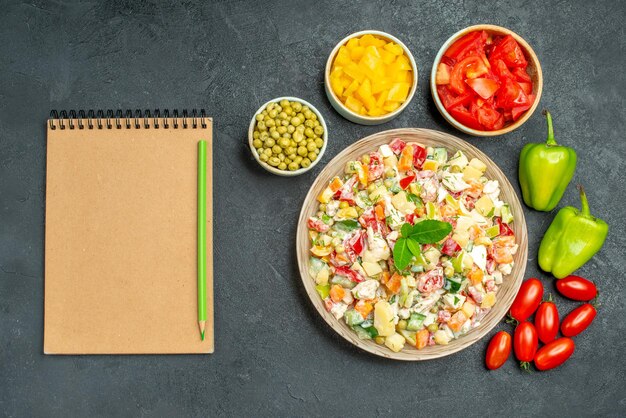 회색 테이블에 연필이 있는 메모장과 그릇에 다양한 야채를 넣은 야채 샐러드