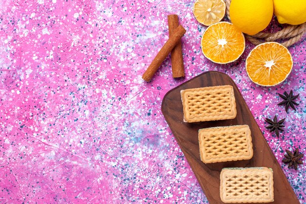 Top close view waffle sandwich cookies with fruit cream filling and tea on light pink desk.