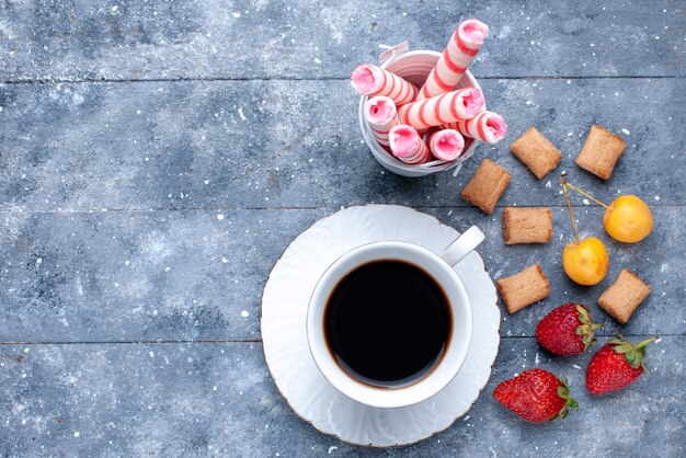 밝은 책상에 딸기 쿠키 핑크 스틱 사탕과 커피 한잔의 상위 가까이보기