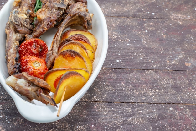 Top closer view of fried meat with greens and baked plums inside plate on brown desk