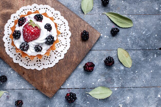 Вид сверху на маленький вкусный торт со сливками и ягодами на свету