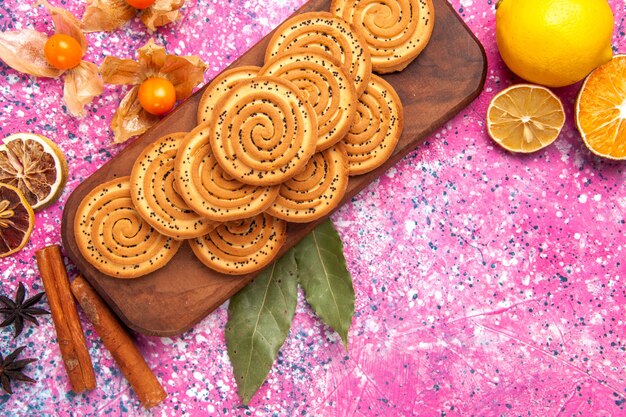 Сверху внимательнее рассмотреть круглое сладкое печенье вкусное маленькое печенье, выложенное корицей и лимоном на розовом столе.