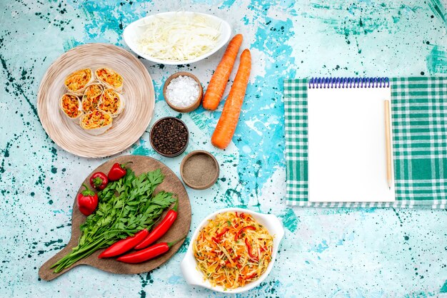 Top closer view of sliced vegetable rolls dough with tasty filling along with greens notepad and red spicy peppers on bright-blue desk