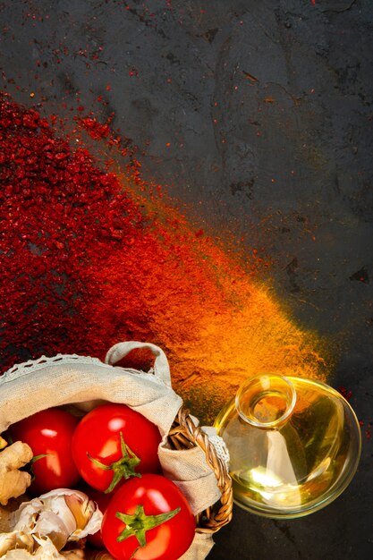 top  colorful spices with a bottle of olive oil and a bunch of tomatoes on black