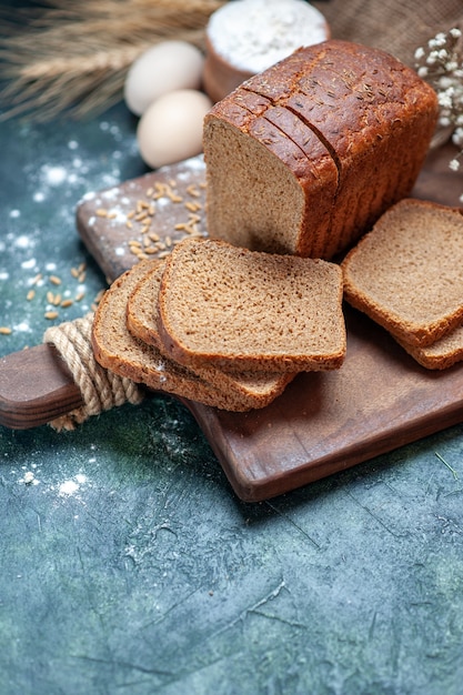 Top of dietary black bread wheats on wooden board spikes flower eggs flour in bowl on blue background