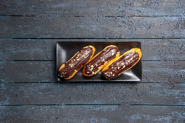 Eclairs al cioccolato vista in lontananza superiore sulla piastra rettangolare su fondo di legno scuro