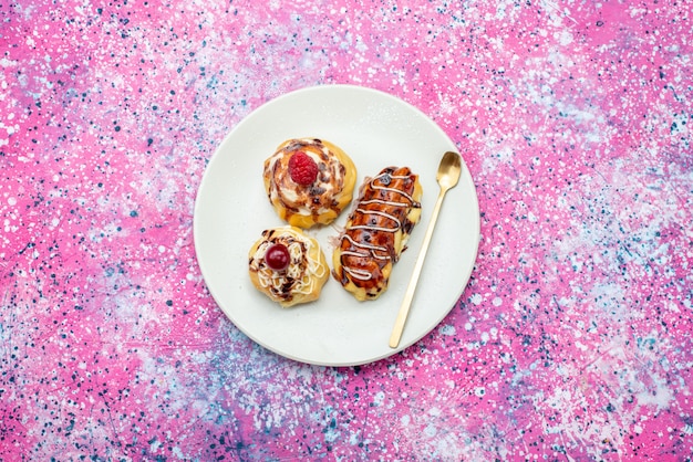 Top distant view delicious fruity cakes with cream and chocolate inside white plate on the pink background cake biscuit sweet bake