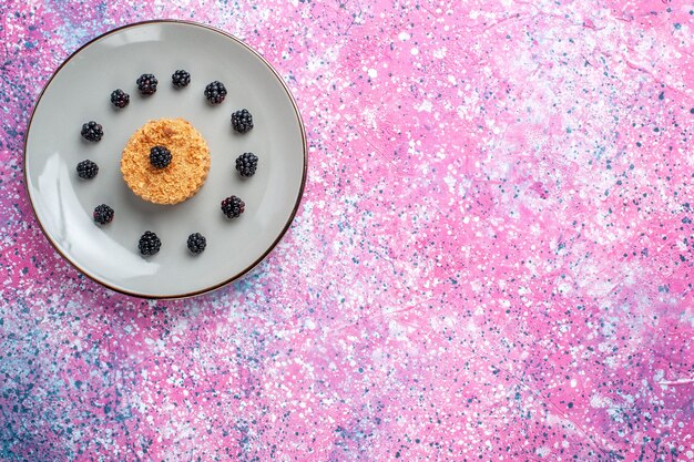 Top distant view of little cake with berries on pink surface