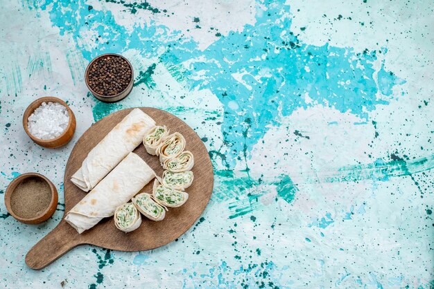 Top distant view tasty vegetable rolls whole and sliced with greens filling and seasonings on bright-blue desk, food meal roll vegetable