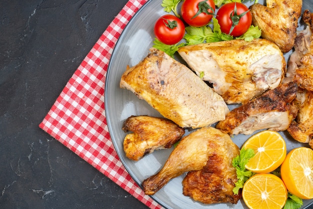 Верхняя половина вида запеченная курица, свежие помидоры, ломтики лимона на тарелке, салфетке на черном столе