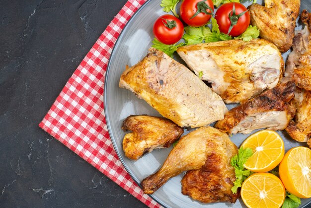 Top half view baked chicken fresh tomatoes lemon slices on plate napkin on black table