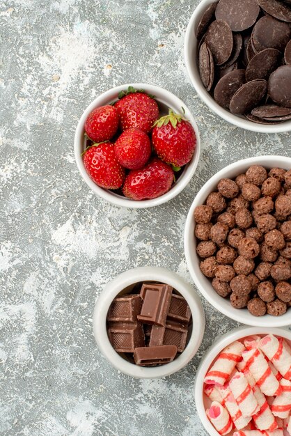 Top half view bowls with candies strawberries chocolates cereals and cacao at the right side of the grey-white ground