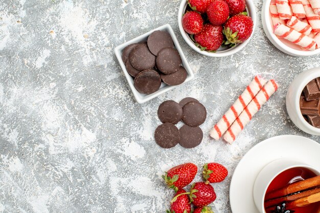 Top half view bowls with strawberries chocolates candies and cinnamon anise seed tea on the grey-white ground