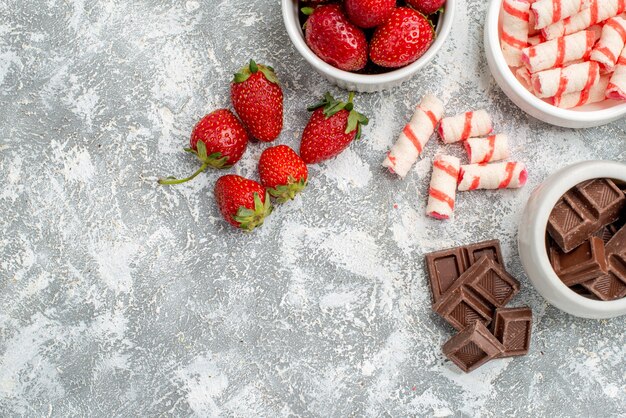 회색-흰색 모자이크 바닥의 오른쪽에 딸기 초콜릿 사탕과 일부 딸기 초콜릿 사탕이있는 상단 절반보기 그릇