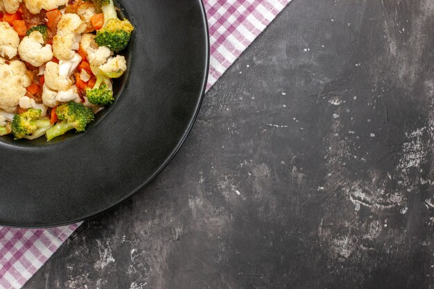 Top half view broccoli and cauliflower salad on black oval plate pink and white checkered tablecloth on dark background free space