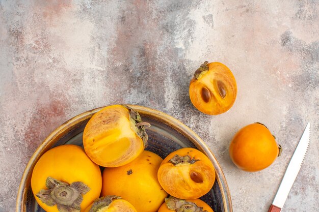 Top half view delicious persimmons in a bowl persimmon and knife on nude background