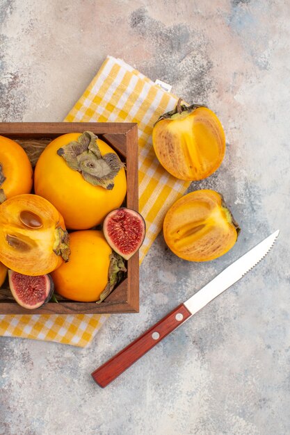 Top half view delicious persimmons and cut figs in wood box a cut persimmon a knife on nude background